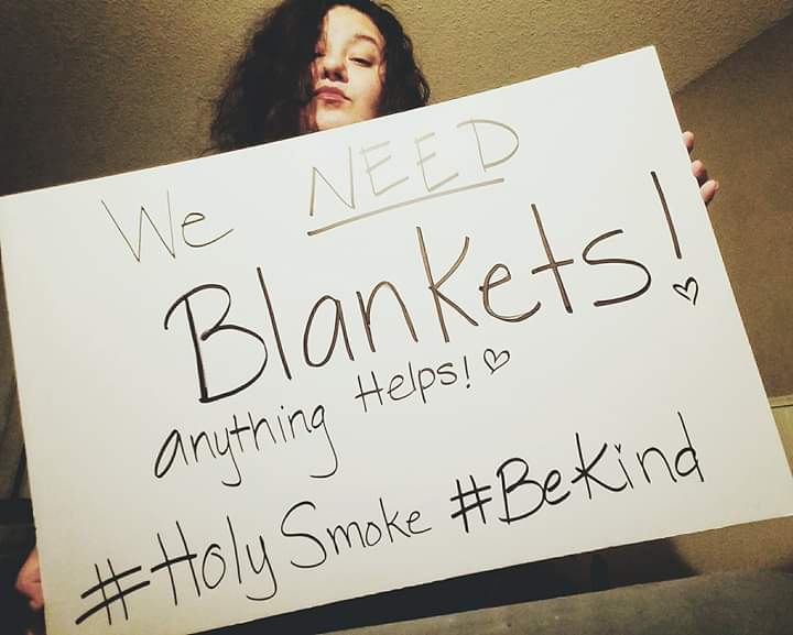 Girl holding sign: /we need blankets! Anything Helps! #Holy Smoke #Be Kind